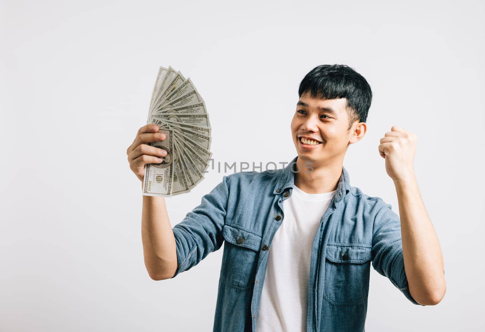 Portrait smiling Asian young man holding a bunch of money and pointing studio shot isolated white background, happiness and excitement man in dollar banknotes celebrating by Sorapop