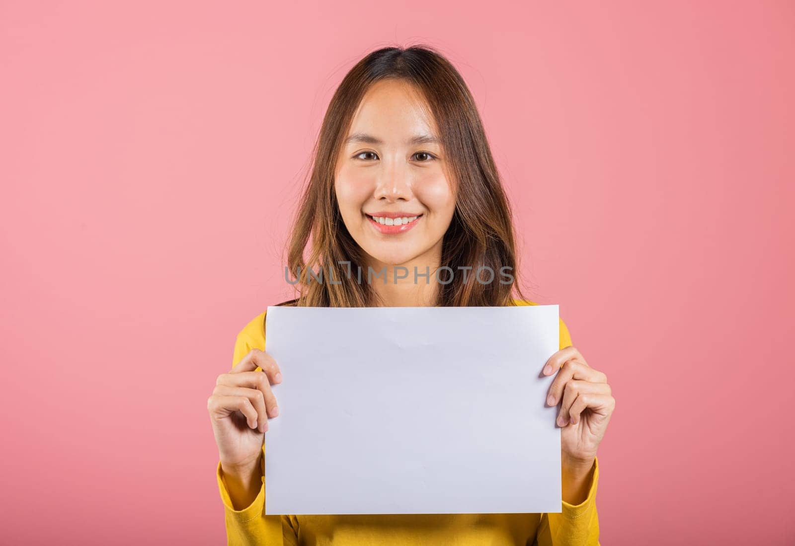 Portrait Asian happy beautiful young woman teen holding a blank sheet of white A4 paper poster for advertising studio shot isolated on pink background by Sorapop