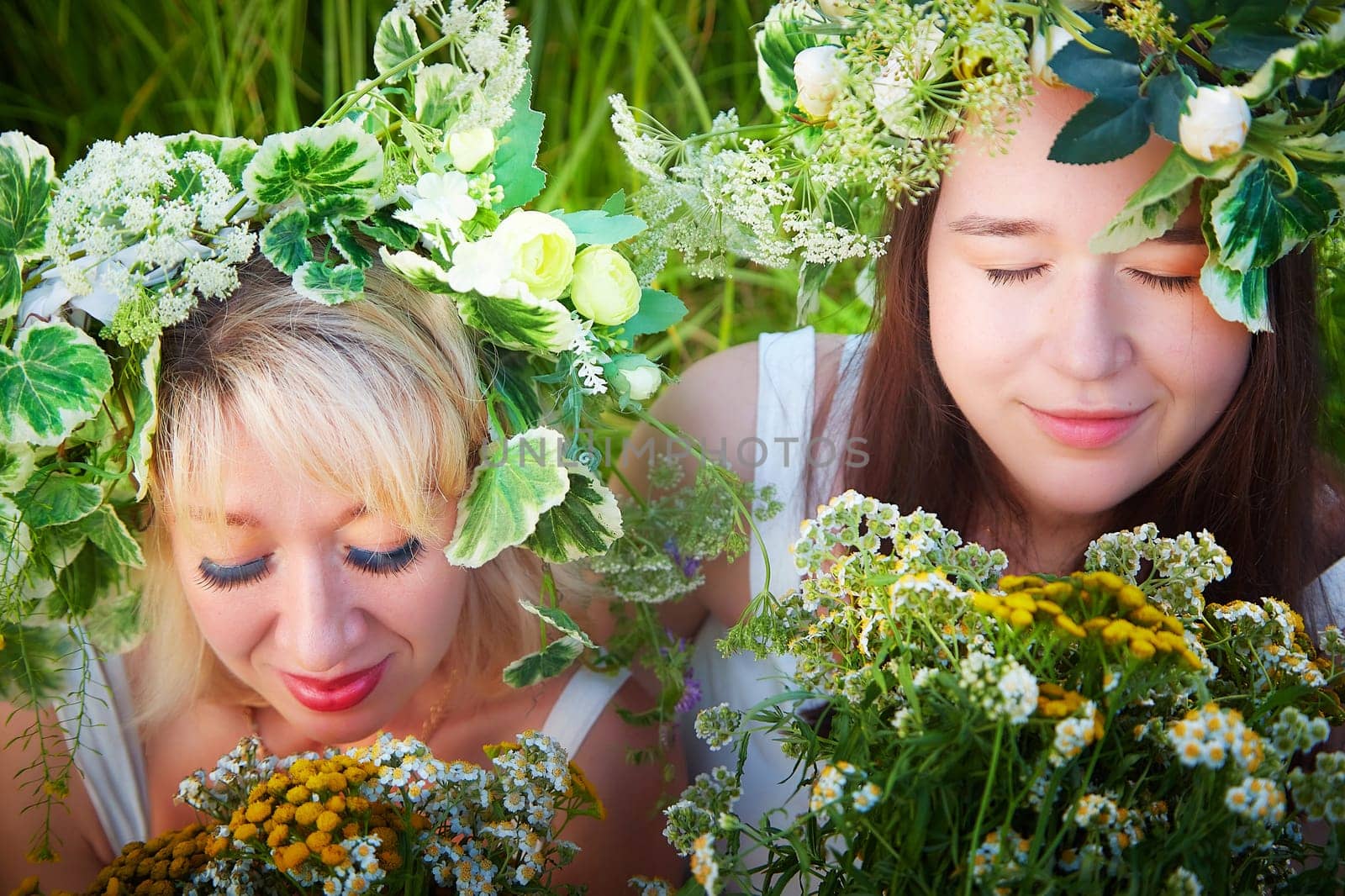 Mother and daughter in white sundresses, wreaths of flowers and bouquet in nature evening at sunset . Family celebrate Slavic Holiday of Ivan Kupala