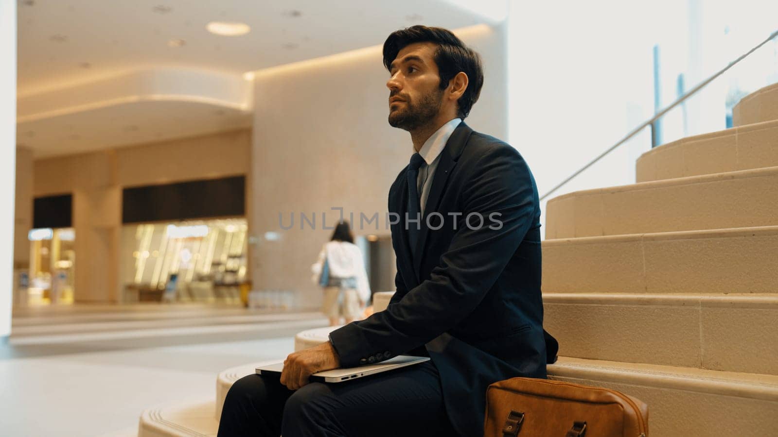 Professional smart business man sitting with bag while holding laptop. Smart project manager sitting and waiting business partner while looking around. Blurred background. Business concept. Exultant.