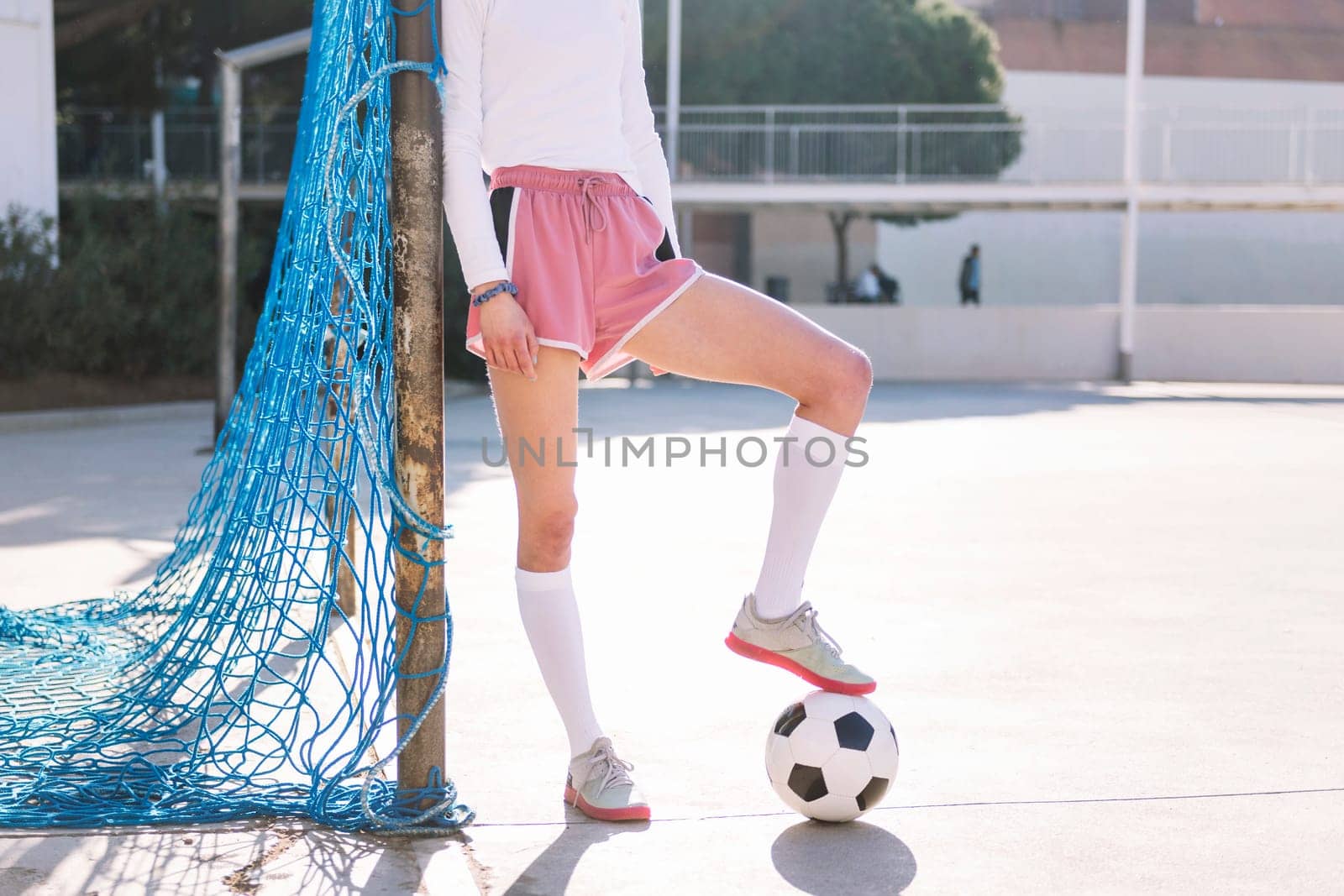 legs of an unrecognizable female football player stepping on a soccer ball next to the goal of an urban court, concept of sport and active lifestyle, copy space for text