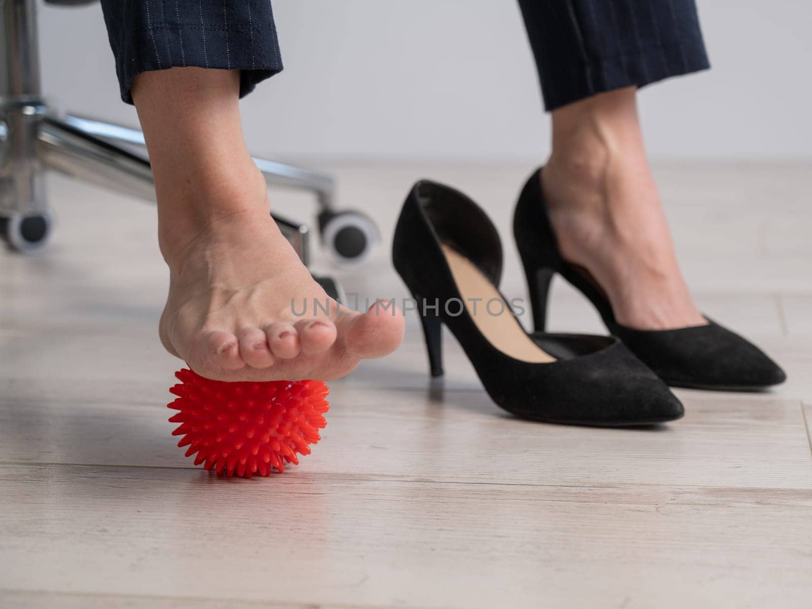 Business woman massages her feet on a massage ball with spikes