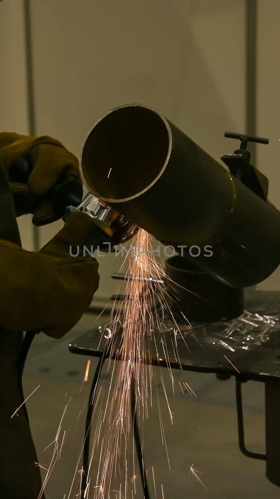 A welder wearing a protective mask cuts a metal pipe. Vertical photo