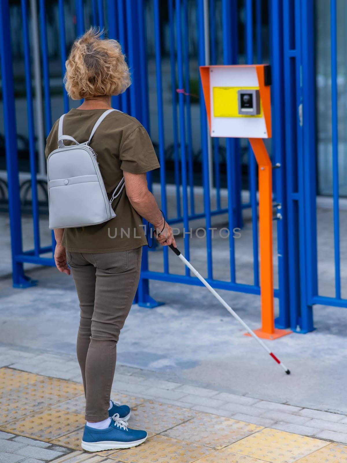 An elderly blind woman goes to a button to call help for people with disabilities. Vertical photo