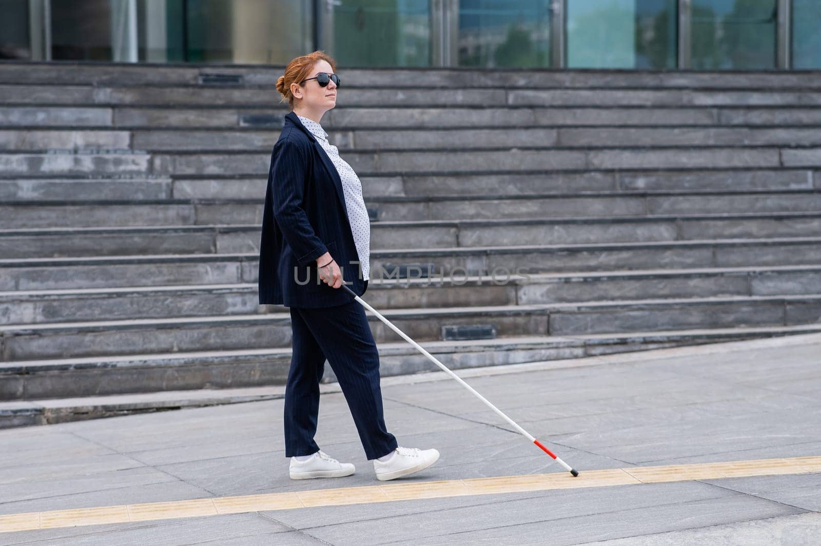 Blind pregnant businesswoman walking along tactile tiles with a cane. by mrwed54