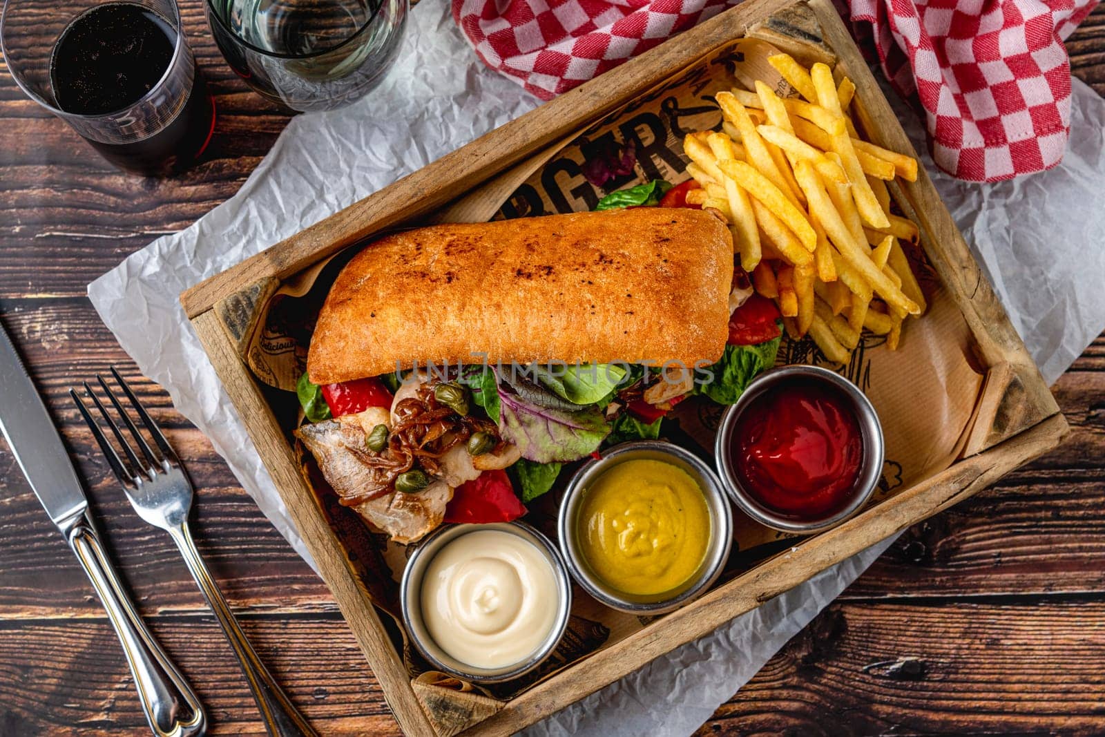Steak sandwich with sauces and french fries on wooden table