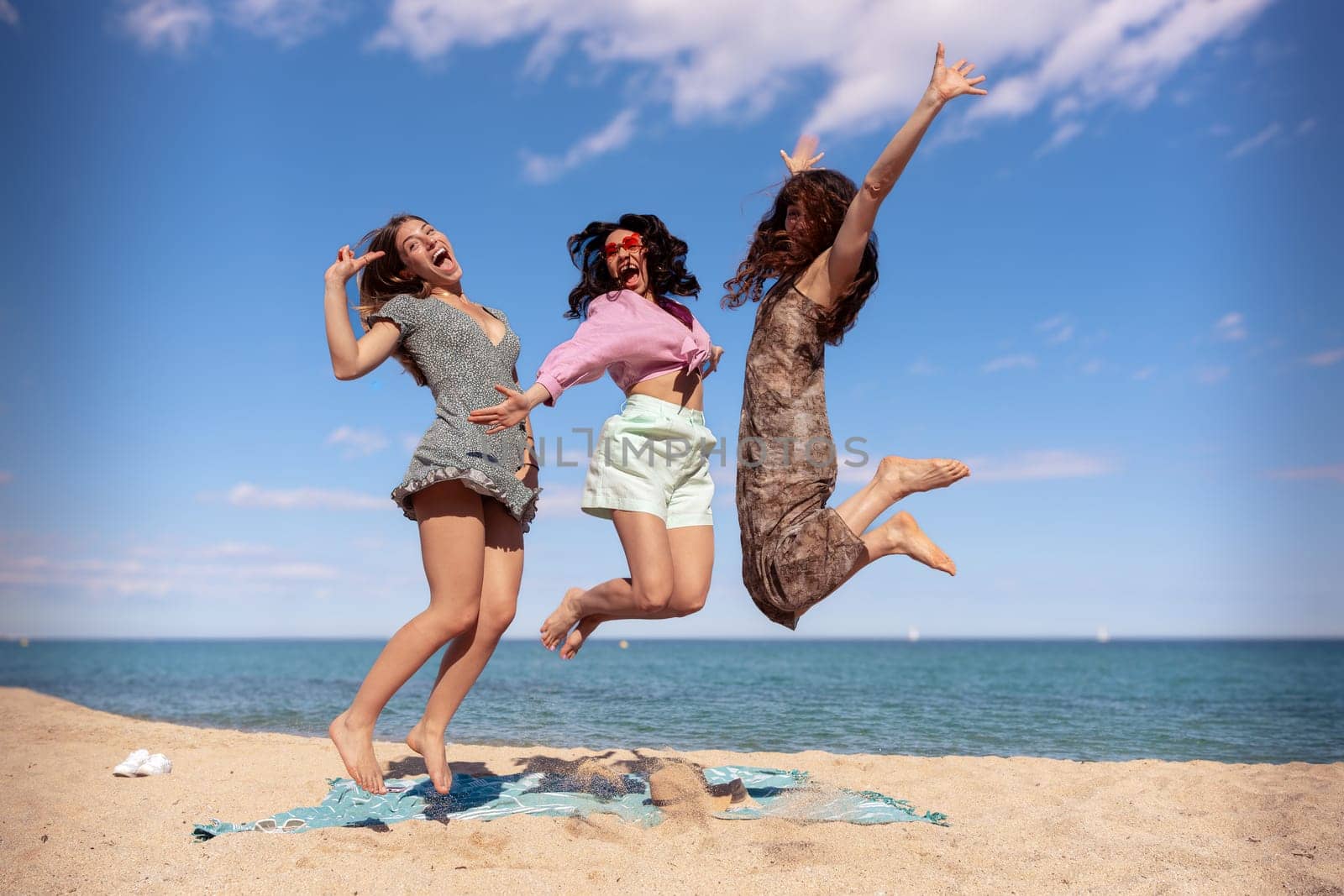 Three happy girls in jumping motion with on the beach outdoors in summer celebrating vacation days. Friends having fun on vacation by the sea carefree, and party concept