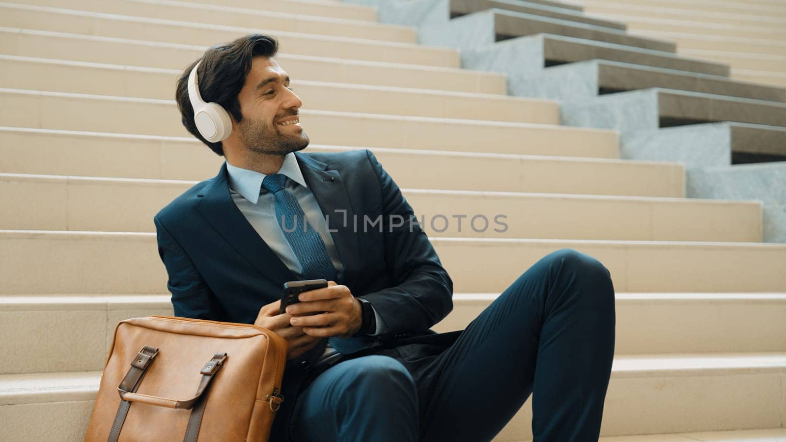 Professional smart business man listening music while lie on stairs. Smart manager happy while receive good news or getting project from headphone. Investor wear suit and bag while sitting. Exultant.