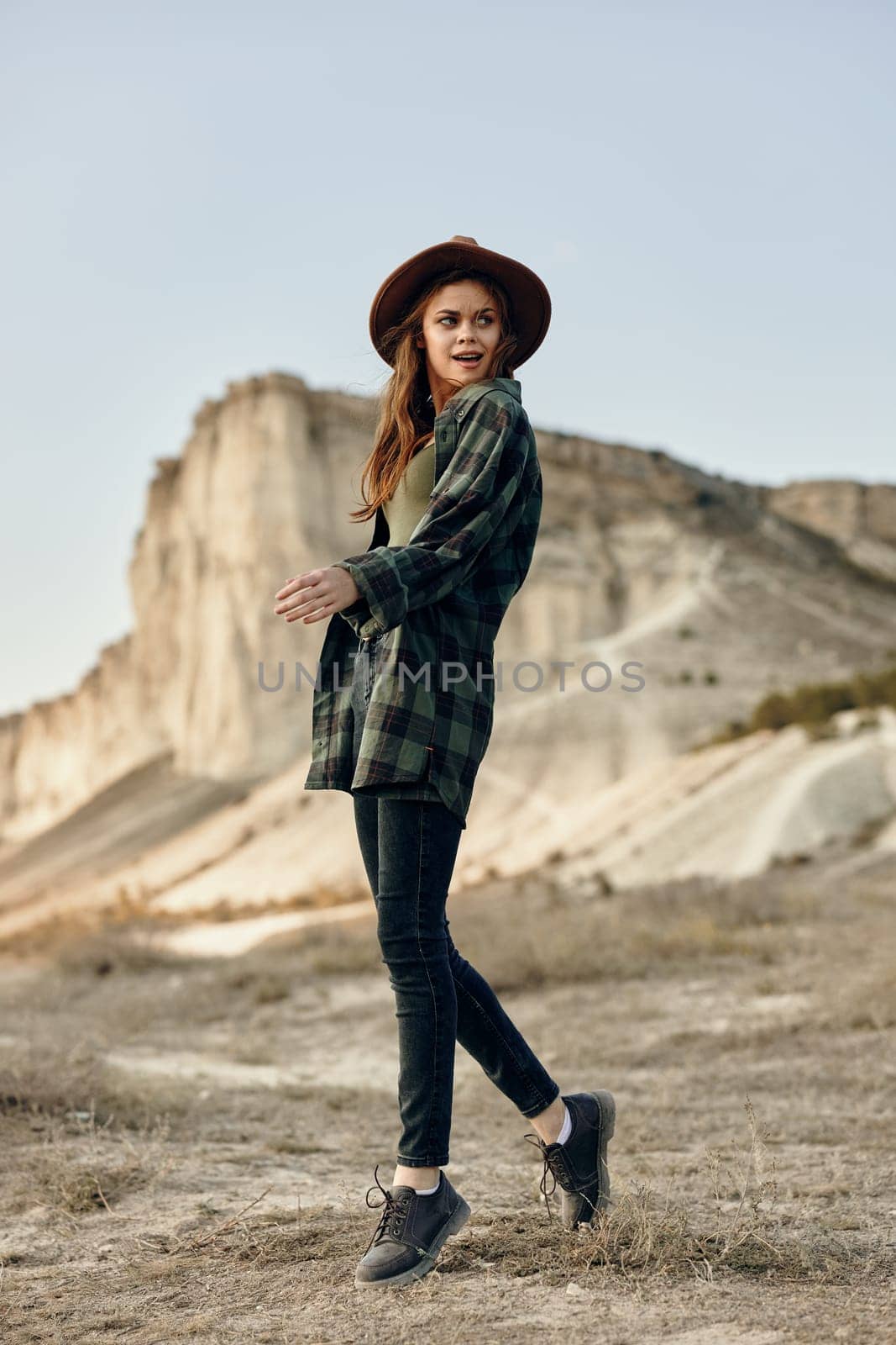 Desert wanderer woman in plaid shirt and hat standing alone in arid landscape by Vichizh