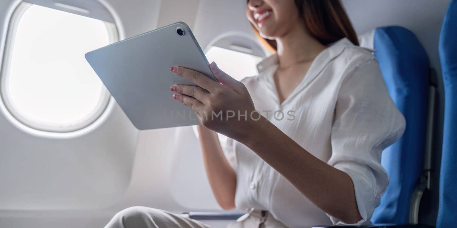 Businesswoman using a tablet on an airplane, showcasing modern corporate travel and productivity in-flight.