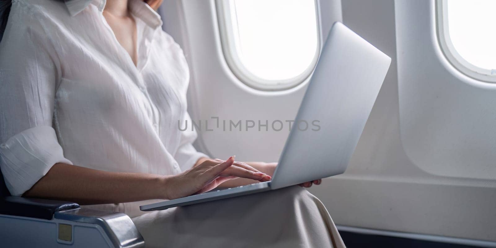 Professional businesswoman working on a laptop during airplane travel, showcasing modern business travel and technology use.