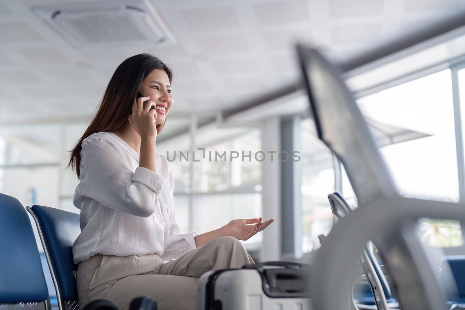 Professional businesswoman at airport terminal, talking on phone, ready for travel. Modern business travel concept with luggage in airport lounge.