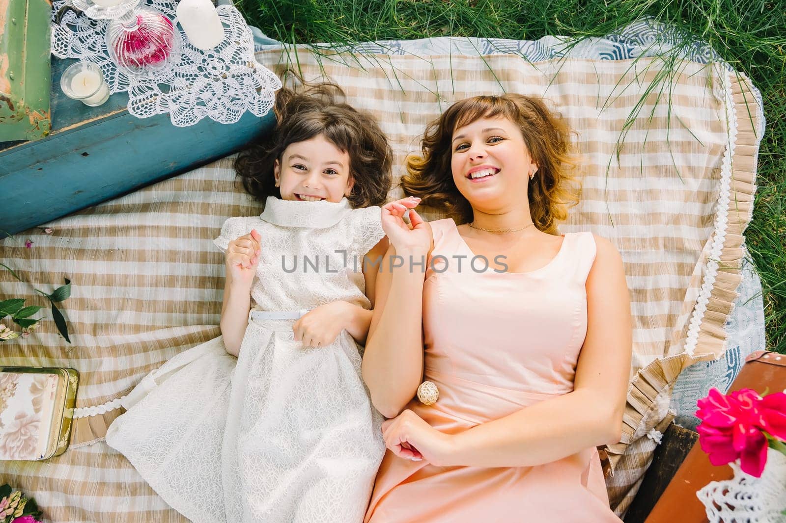 happy mother and daughter playing and smiling while lying on a blanket in the Park in the summer