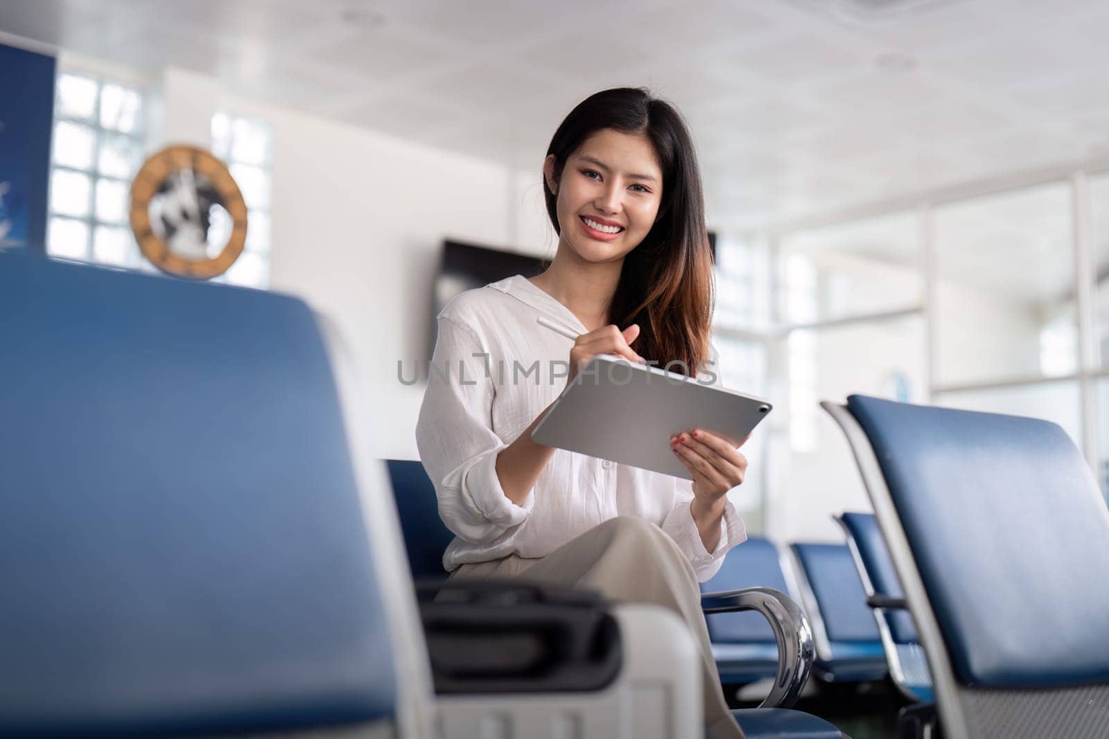 Confident businesswoman using a tablet in an airport lounge, showcasing modern business travel and professional efficiency.