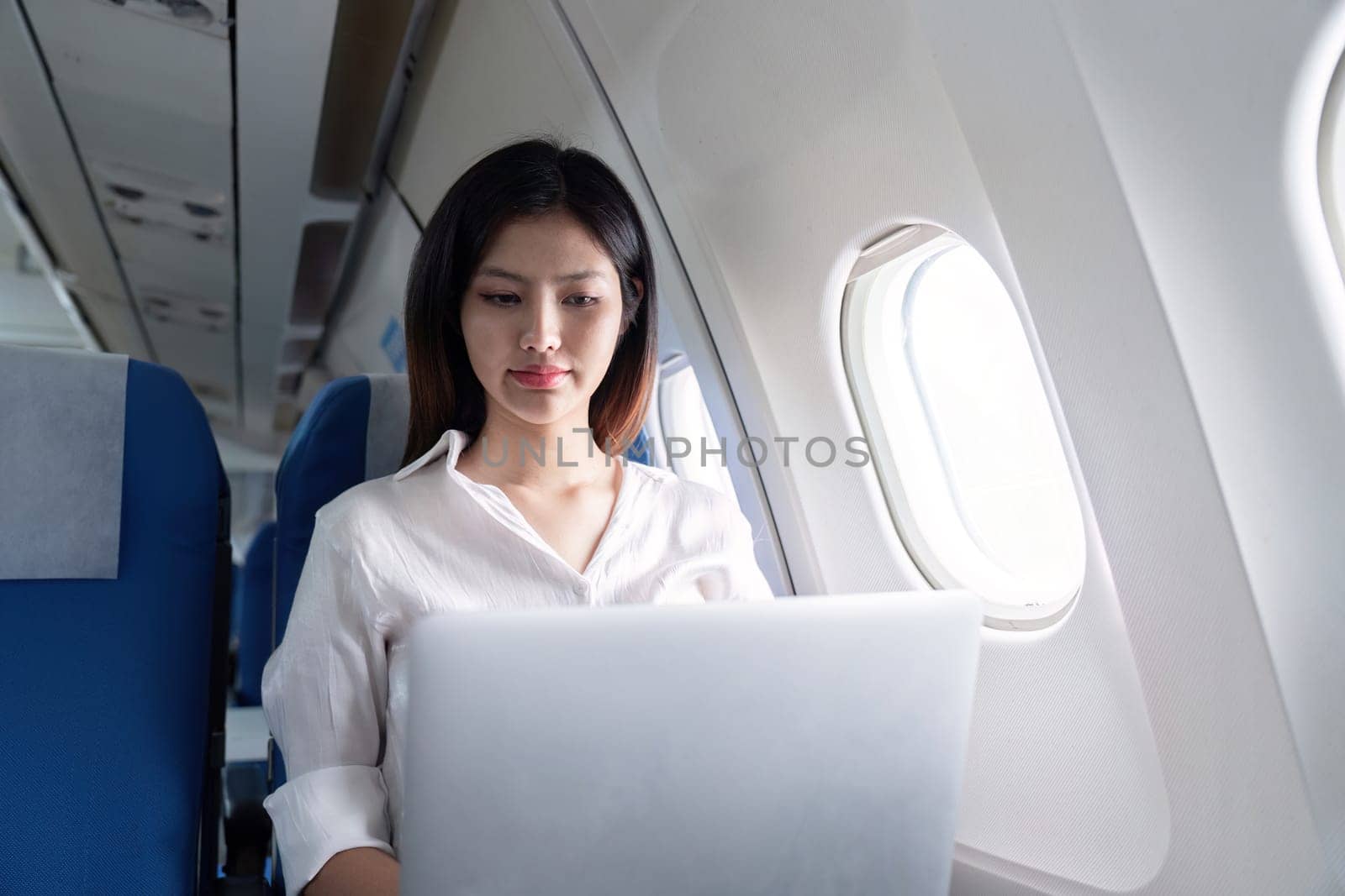 Professional businesswoman working on a laptop during an airplane flight, showcasing modern corporate travel and in-flight productivity.