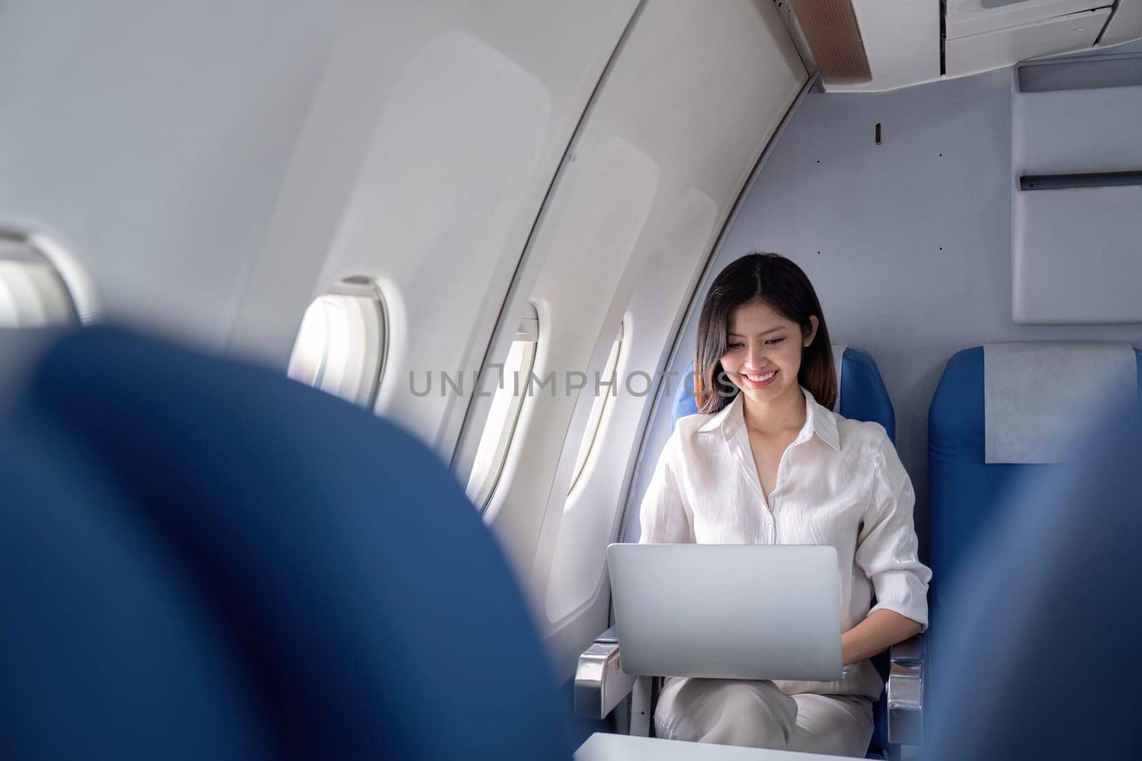Professional businesswoman working on a laptop during airplane travel, showcasing modern corporate travel and connectivity.