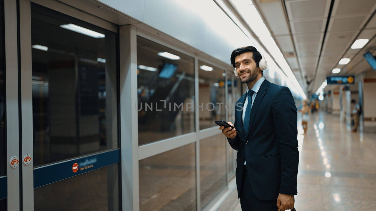 Manager wearing headphone at train station while holding mobile phone. Exultant. by biancoblue