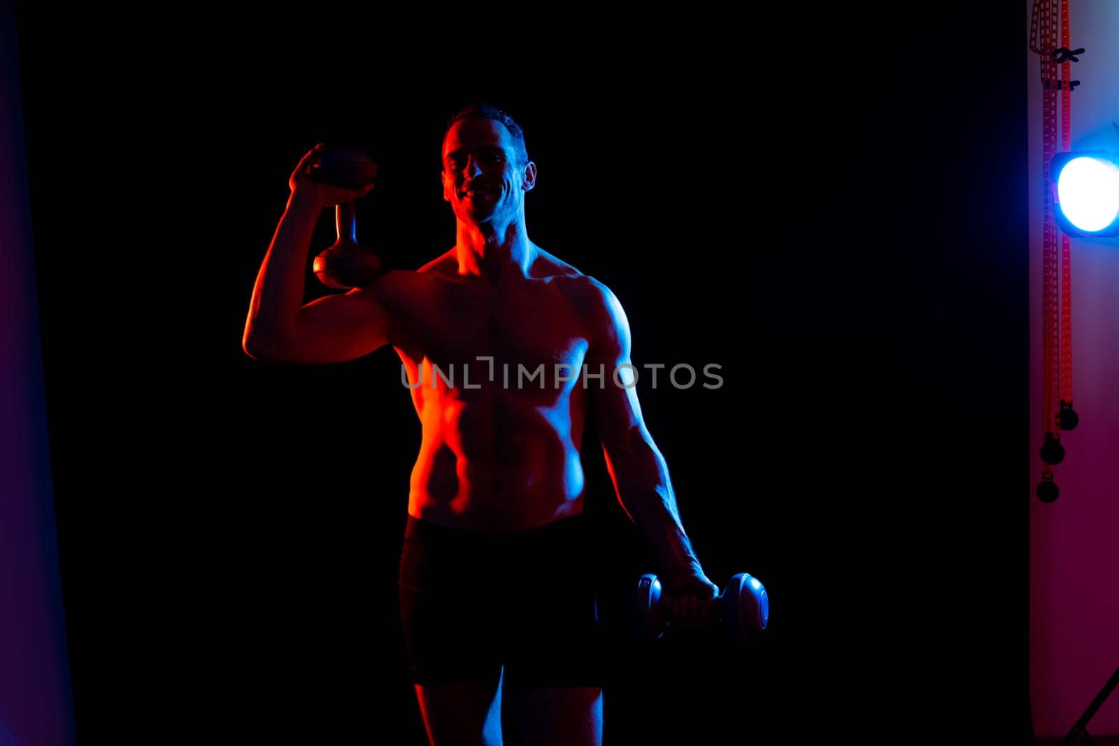 Adult muscular man smiling and screaming while working out hard with a dumbbells.