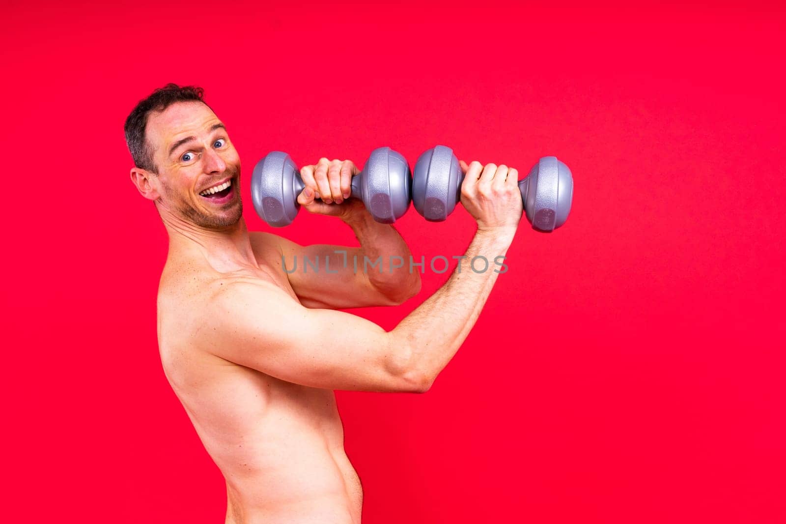 Adult muscular man smiling and screaming while working out hard with a dumbbells.