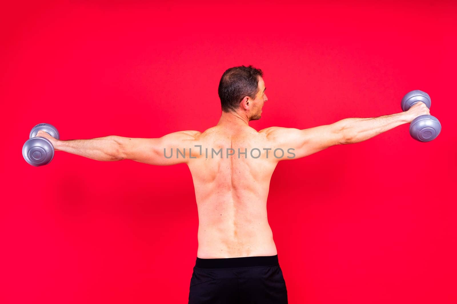 Adult muscular man smiling and screaming while working out hard with a dumbbells.