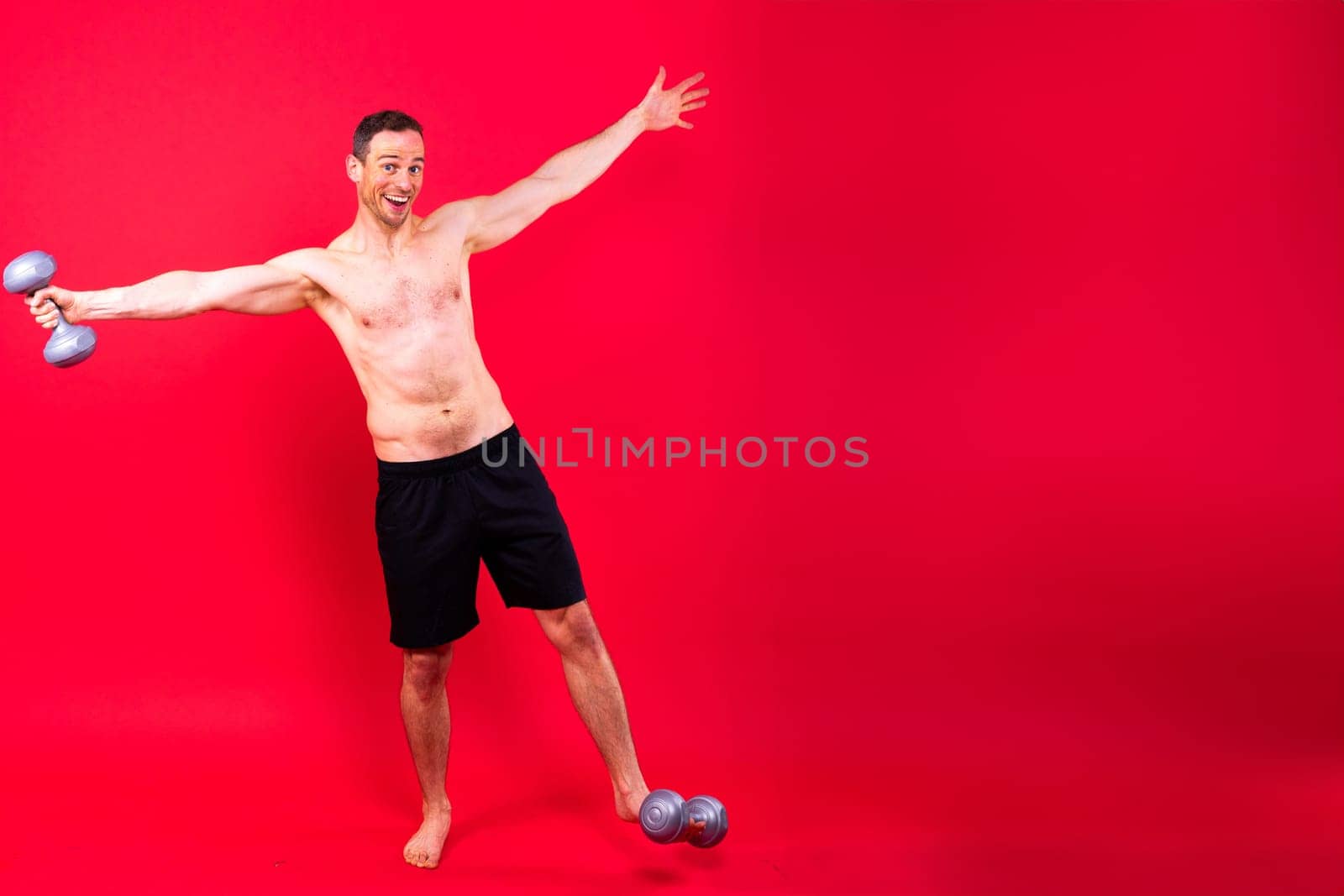 Adult muscular man smiling and screaming while working out hard with a dumbbells.