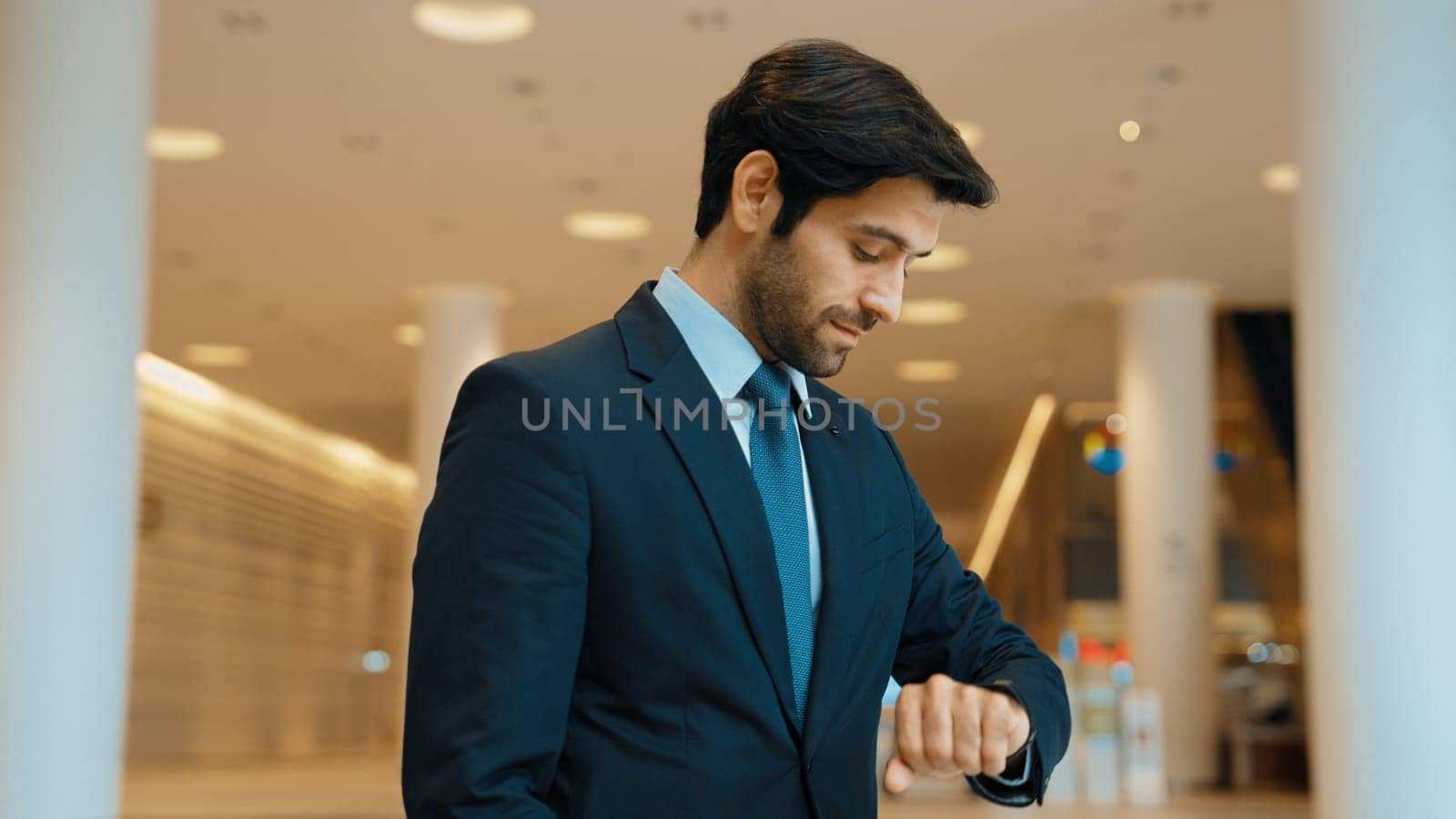 Caucasian smart business man looking at watch while waiting colleague. Executive manager wearing suit while standing at mall with blurred background. Investor wear blue suit check time. Exultant.