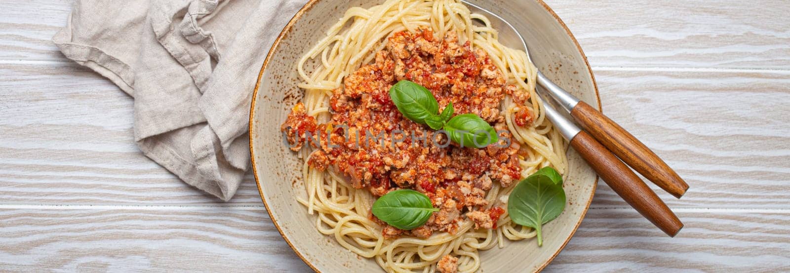 Plate of delicious spaghetti bolognese with fresh basil leaves, served on a rustic wooden table