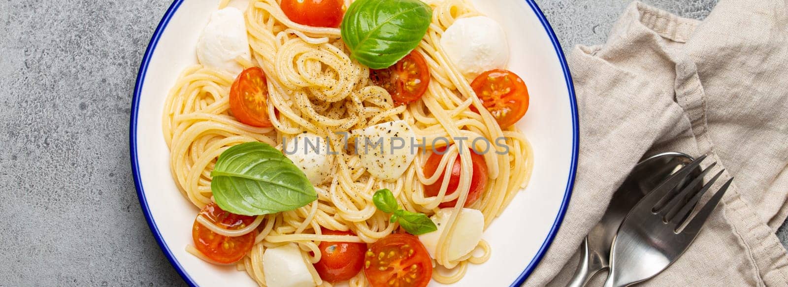 Delicious and fresh spaghetti with cherry tomatoes and mozzarella cheese, seasoned with pepper and basil, served on a plate