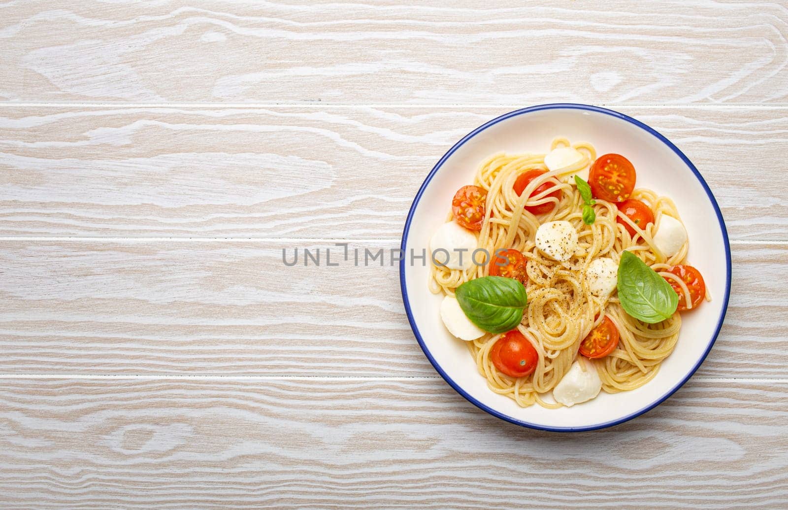 Plate of spaghetti pasta with cherry tomatoes and mozzarella cheese on white wooden background with copy space by its_al_dente