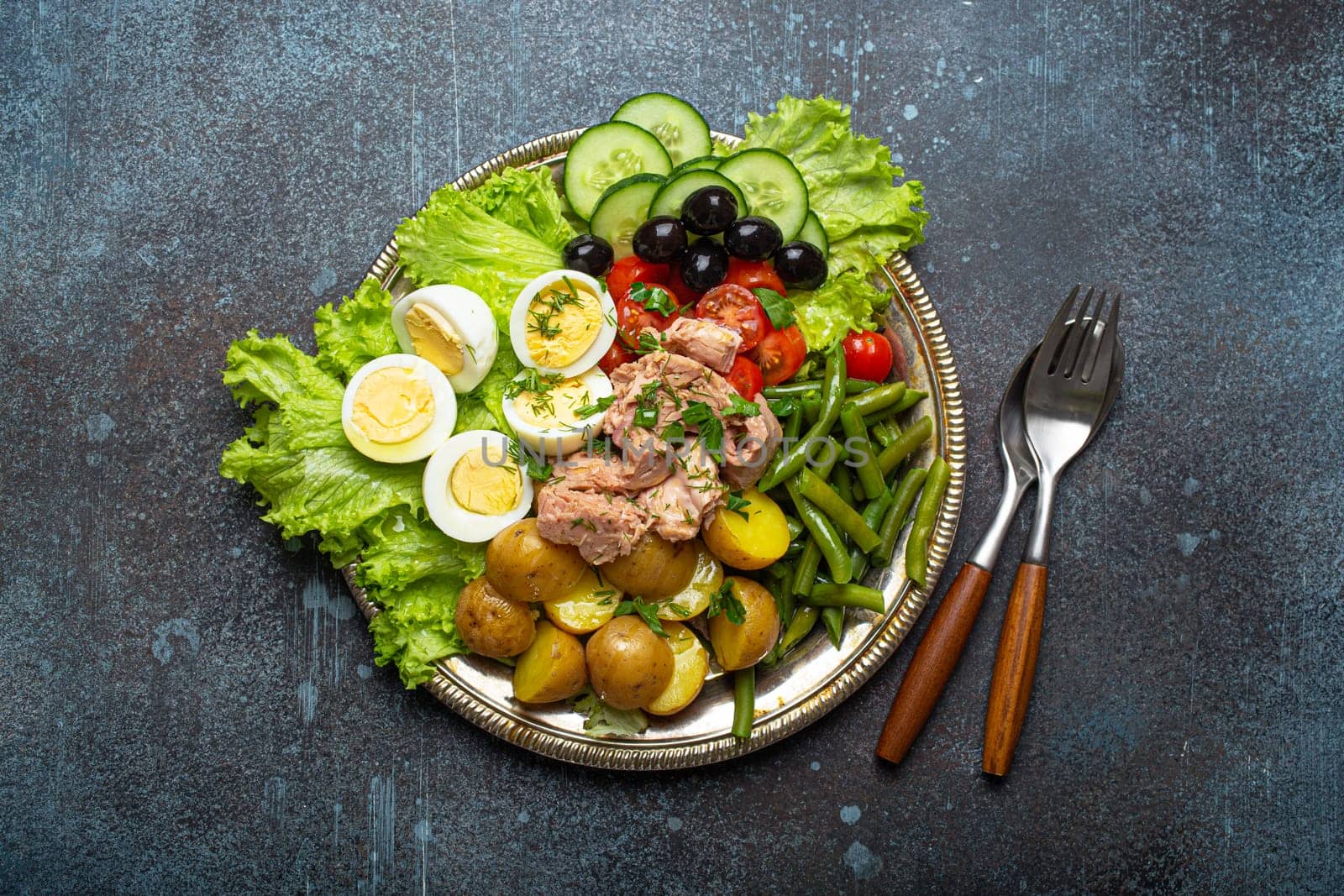 Classic French Nicoise salad with tuna, eggs, potatoes, green beans and olives on a silver platter