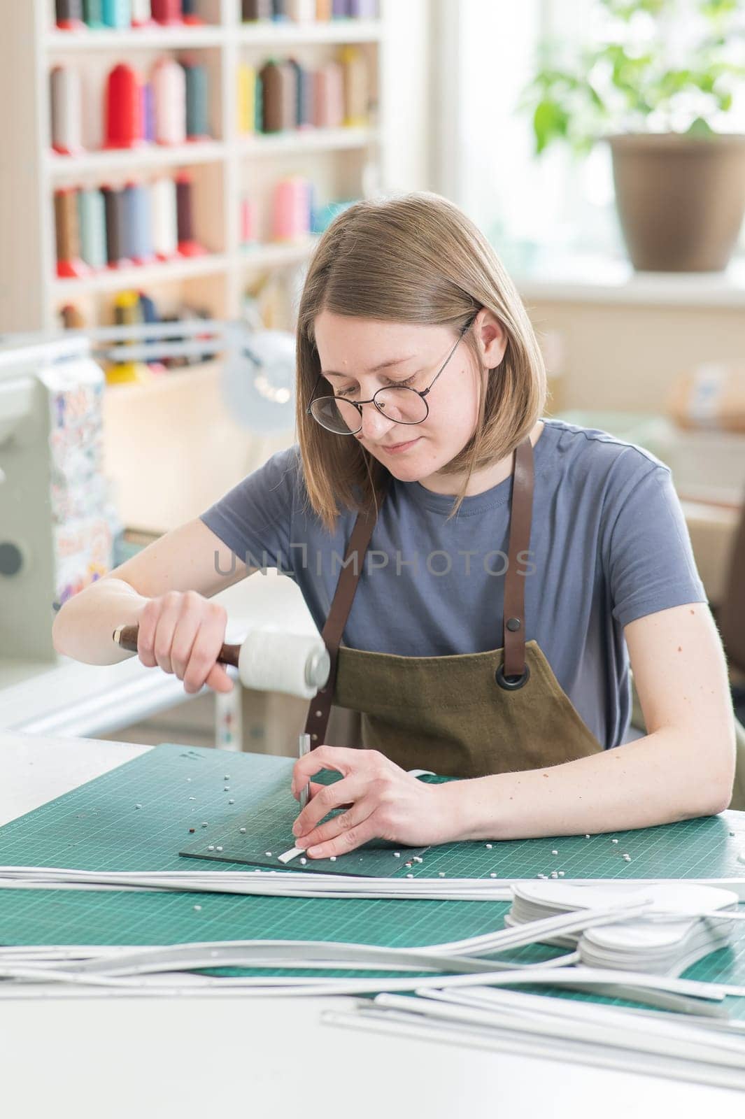 A woman makes holes in a leather belt in a workshop. Vertical photo. by mrwed54