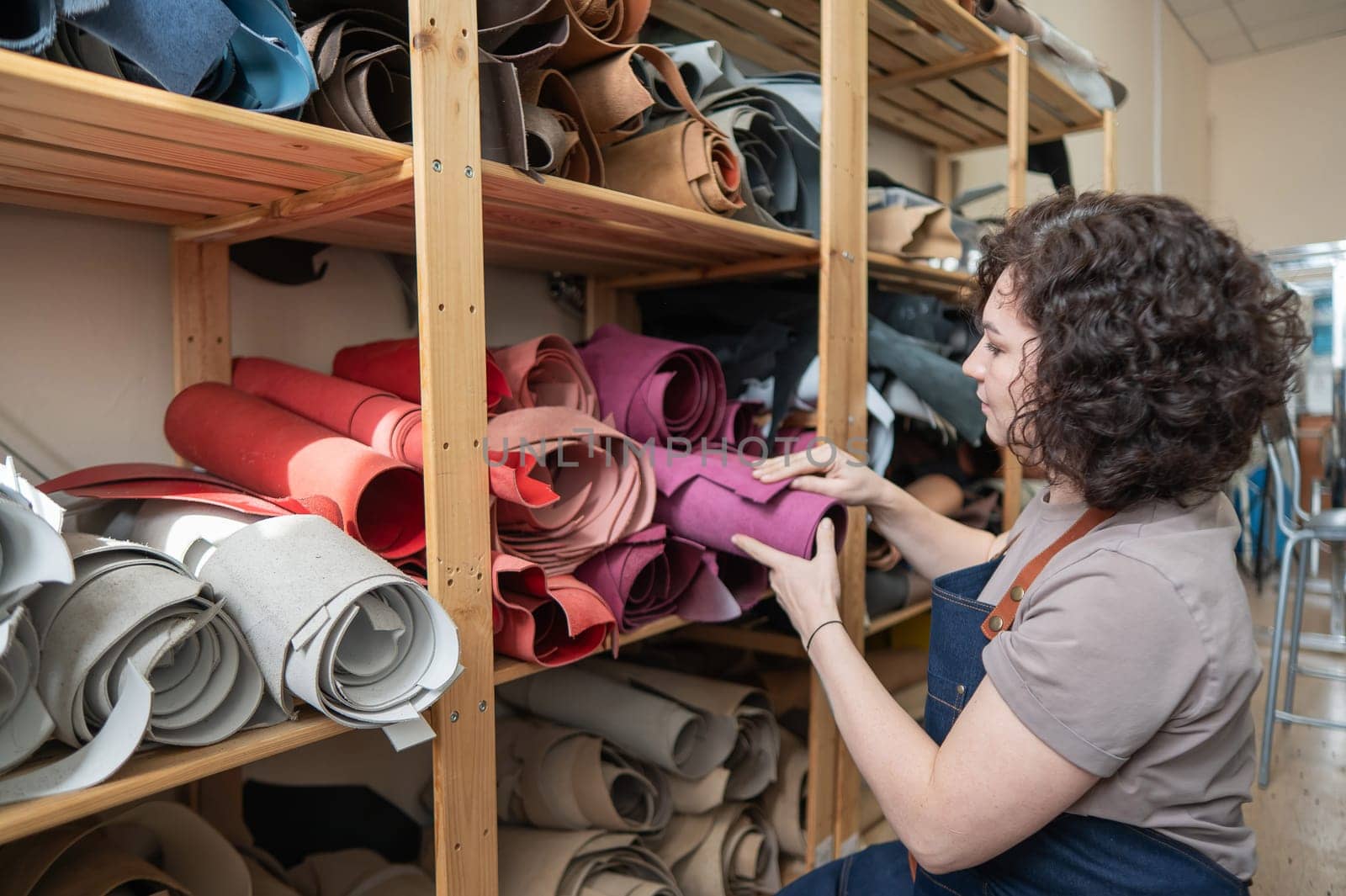 Woman leatherworker selects a roll of leather in the workshop