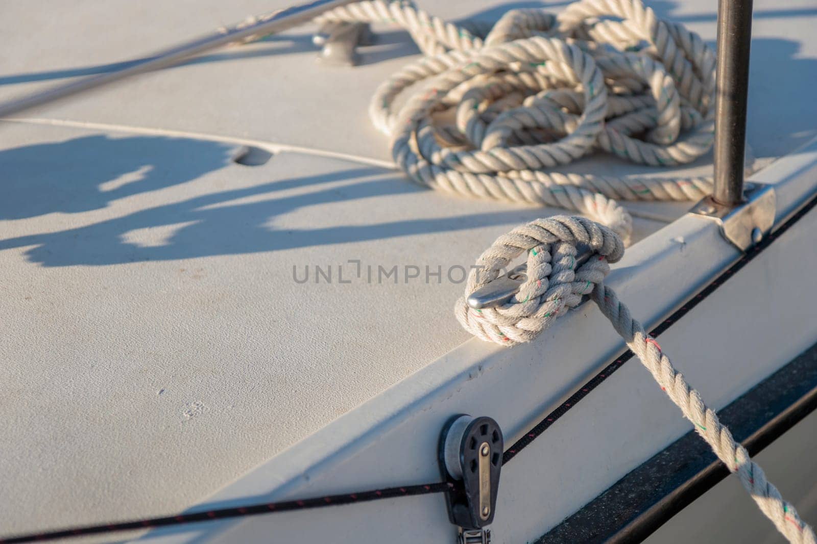 White rope tied to the mooring cleat of a sailboat, sunny light by Gudzar