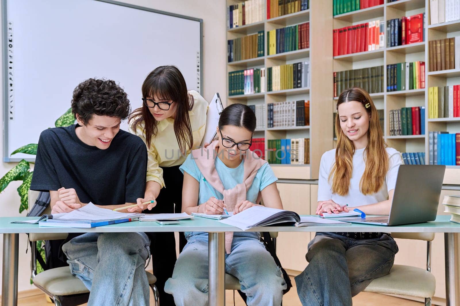 Group of teenage students with female teacher study inside classroom library by VH-studio