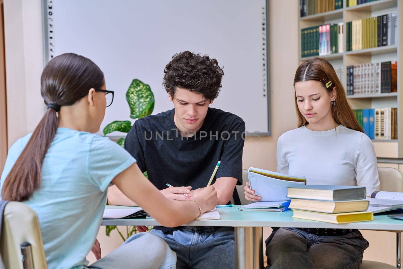 Group of high school students are studying in library class, classmates are laughing talking discussing together, team study project, preparing for tests and exams. Education adolescence communication