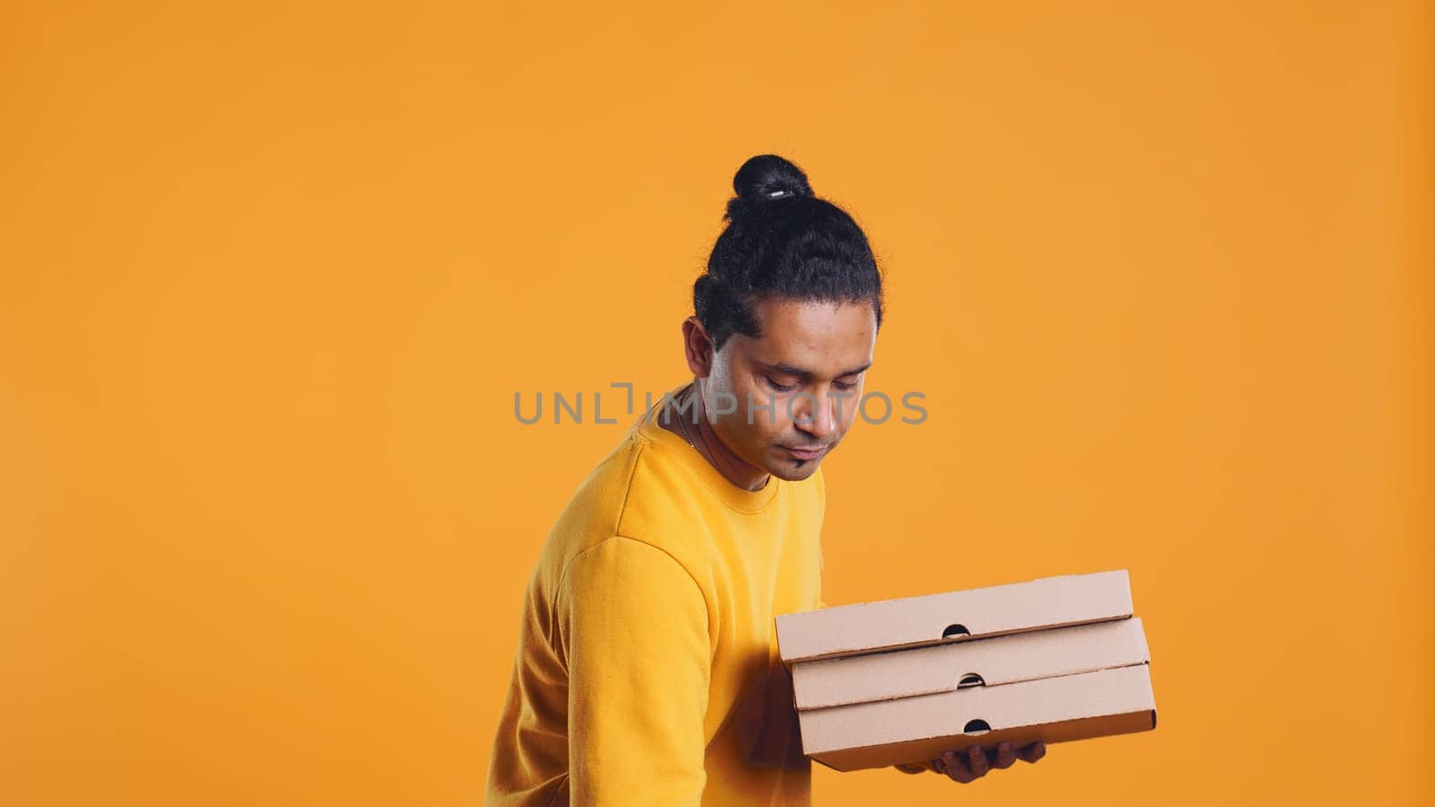 Portrait of indian pizza delivery man holding takeaway orders for customer. Upbeat courier with lunch boxes in arms and thermal food backpack, isolated over studio background, camera B