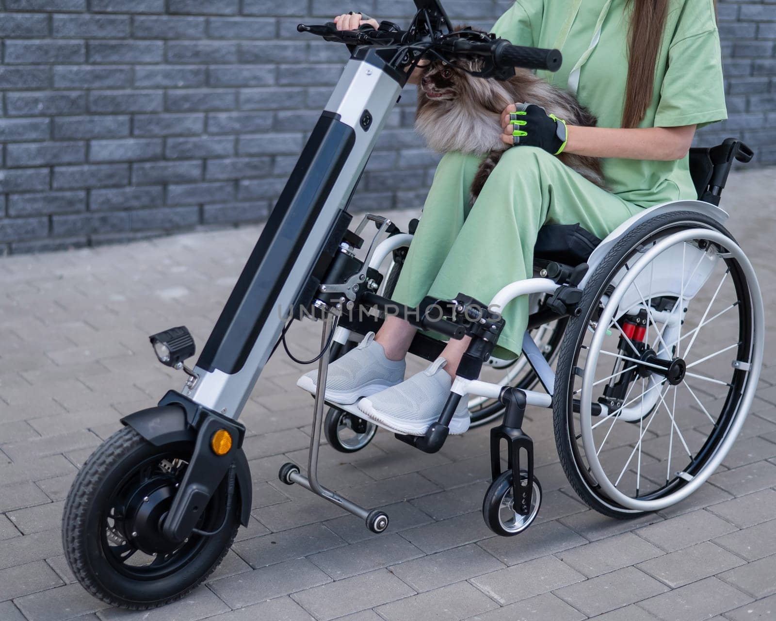 A woman in a wheelchair with a hand-control assist device carries a Spitz merle dog. Electric handbike. by mrwed54