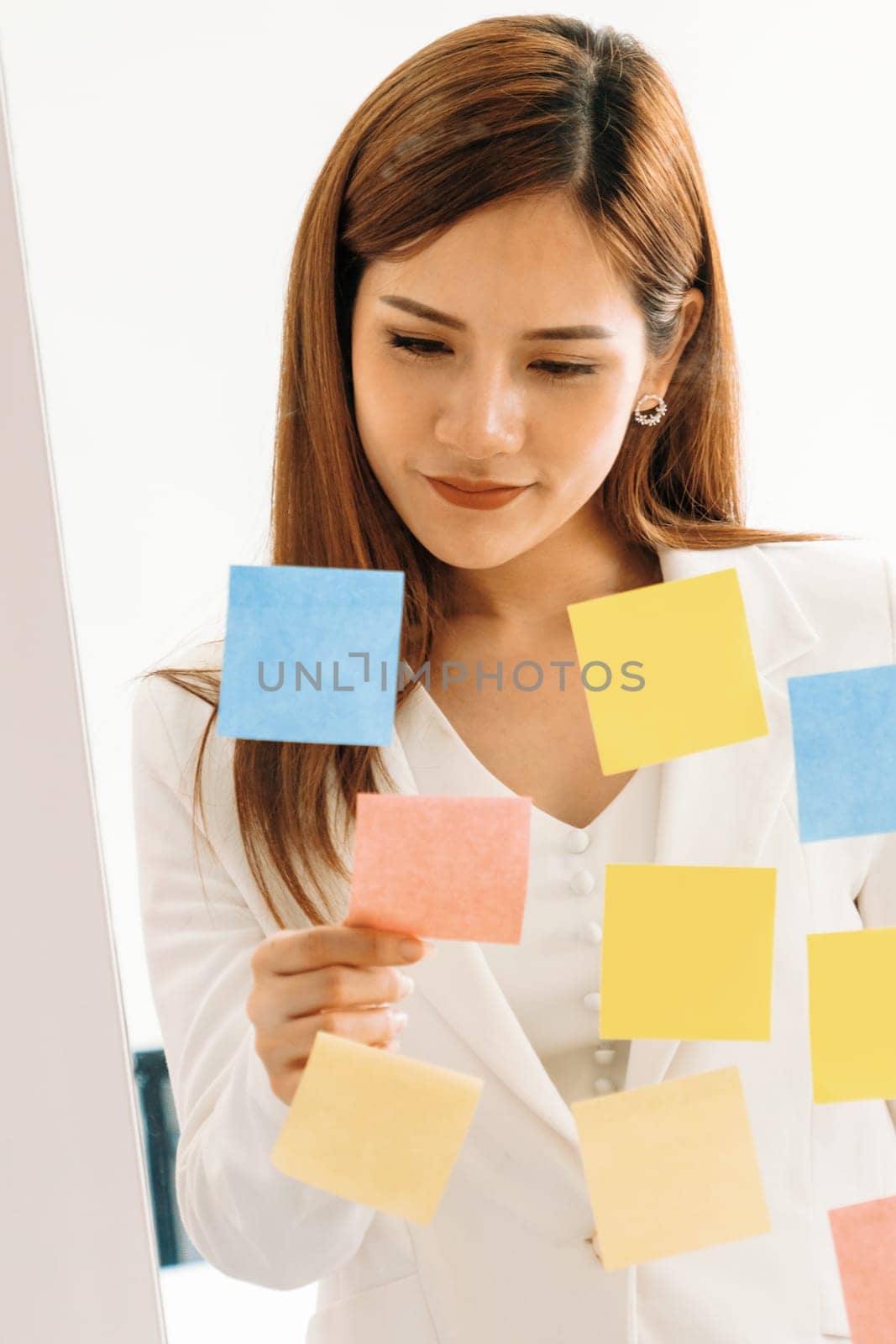 Happy businesswoman thinking creative ideas with sticky notes on glass wall at the office. Work planning and education concept uds