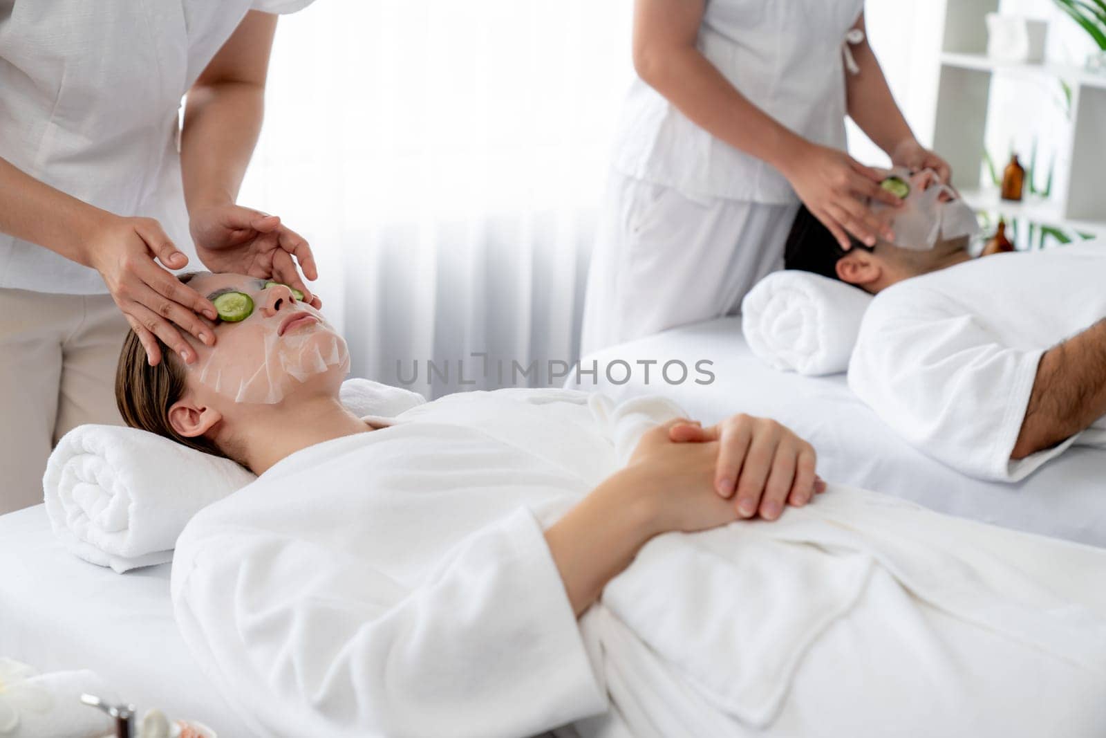 Serene daylight ambiance of spa salon, couple customer indulges in rejuvenating with luxurious cucumber facial mask. Facial skincare treatment and beauty care concept. Quiescent