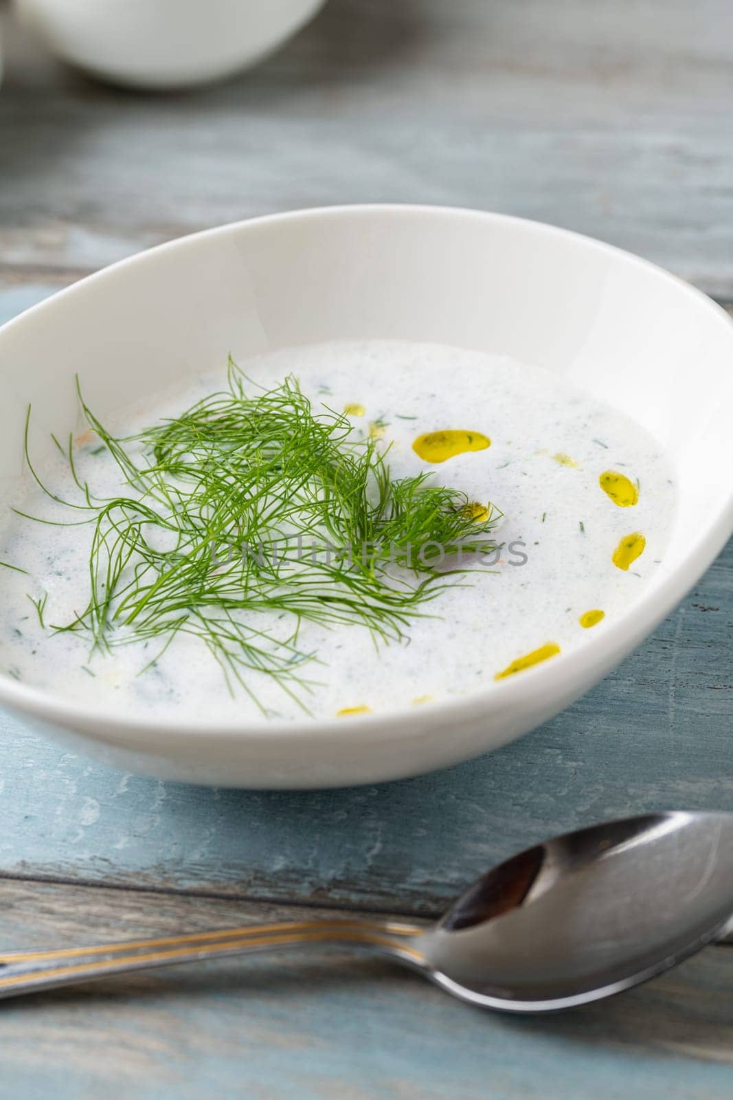 Turkish Cacik or tzatziki (caciki) on white porcelain plate on wooden table by Sonat