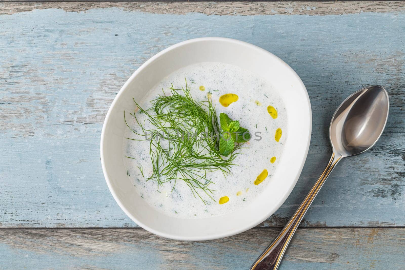 Turkish Cacik or tzatziki (caciki) on white porcelain plate on wooden table by Sonat