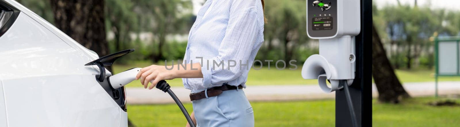 Young woman recharge EV electric vehicle battery from EV charging station. Exalt by biancoblue