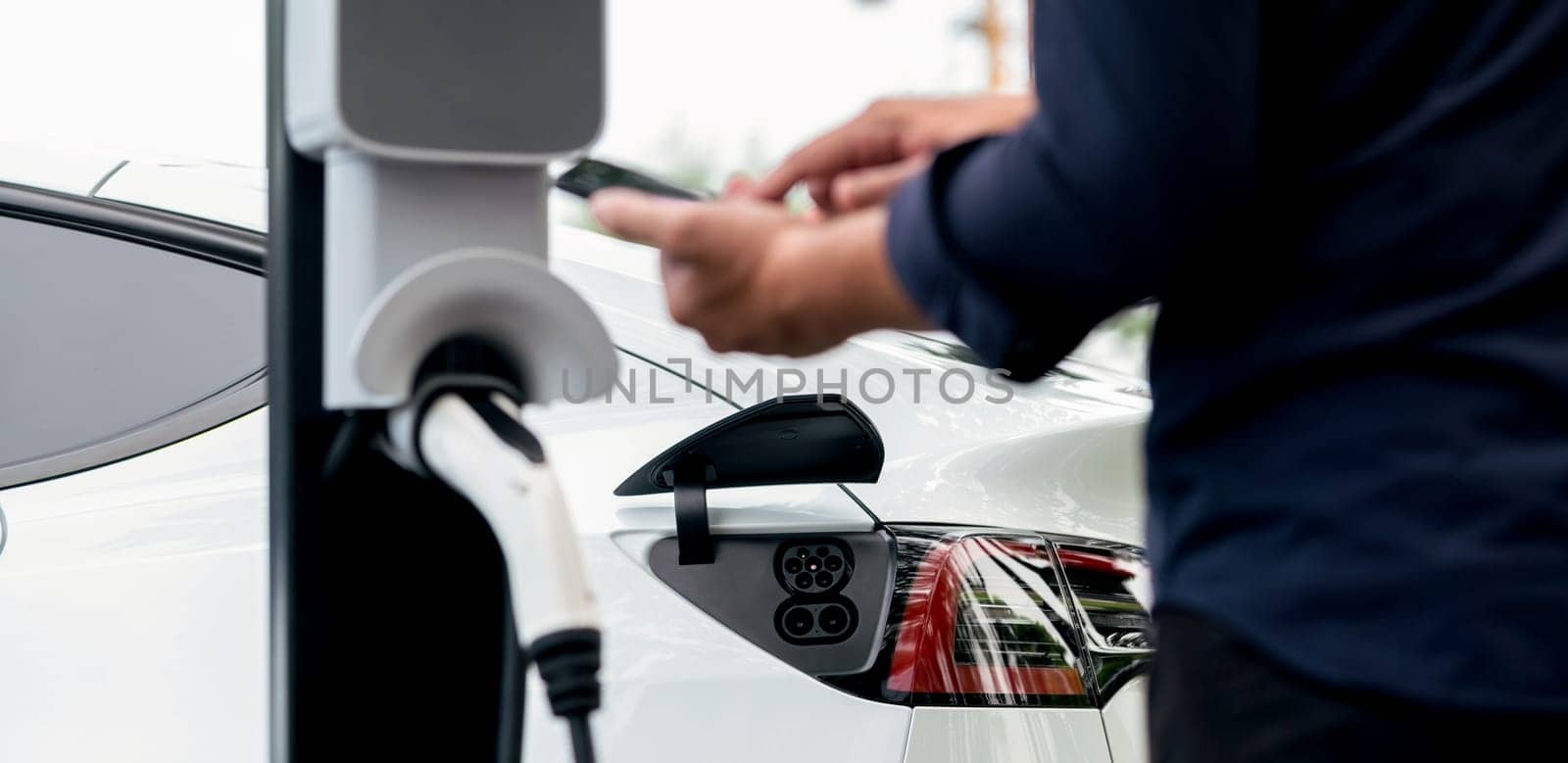 Man using smartphone to pay for electric car charging. Exalt by biancoblue