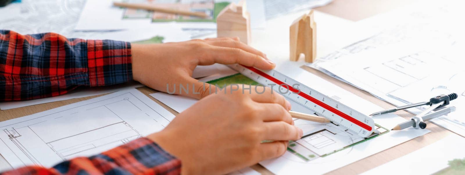 Closeup of architect engineer hand using ruler to mature and draw a blueprint on meeting table with wooden block, pencil and blueprint scatter around at architectural modern office. Delineation.