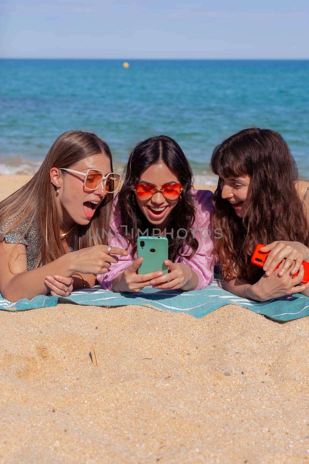 Three happy young friends on the beach using apps on their smartphones.Vertical by mariaphoto3