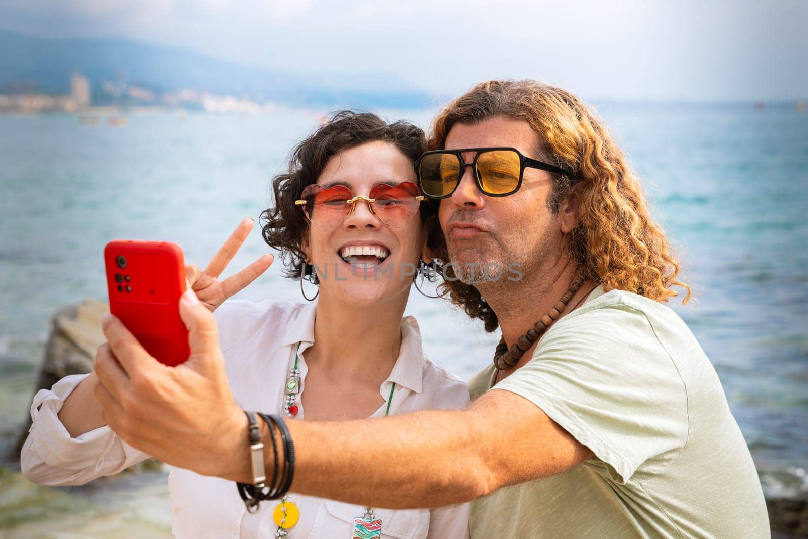 Beautiful youngcouple on the beach taking a selfie surfing with smartphone by mariaphoto3