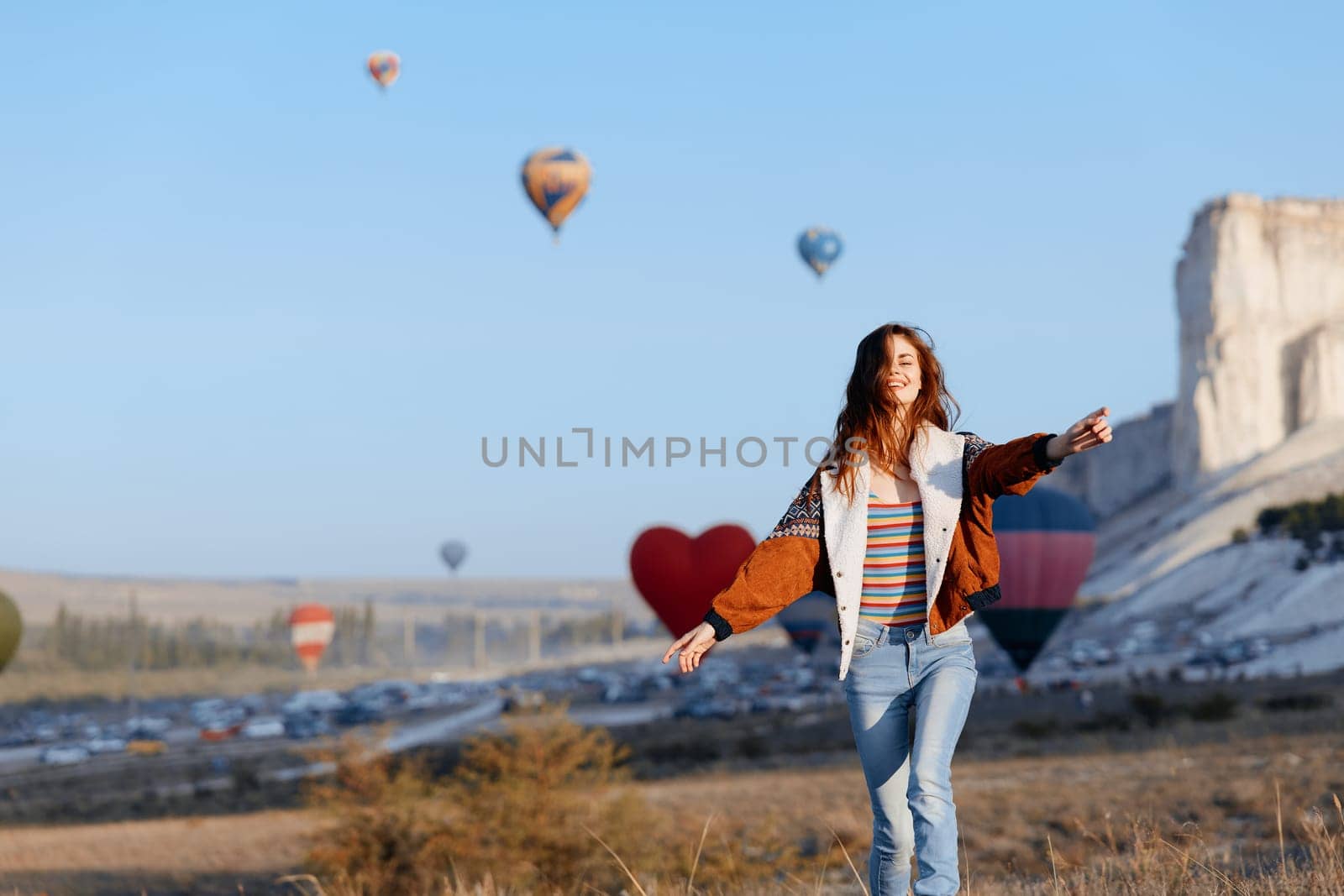 Woman admiring colorful hot air balloons against majestic mountain backdrop
