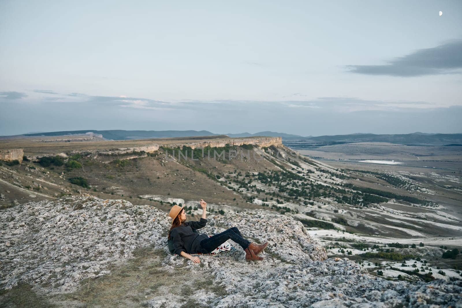 Serene woman sitting on rocky mountaintop overlooking vast valley landscape