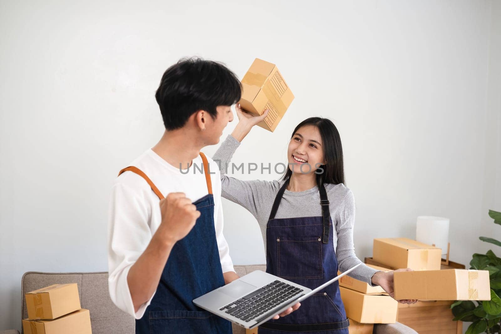 A cheerful couple working together in their home office, packing boxes and managing their online business. They are wearing aprons and holding packages, showcasing their e-commerce venture.