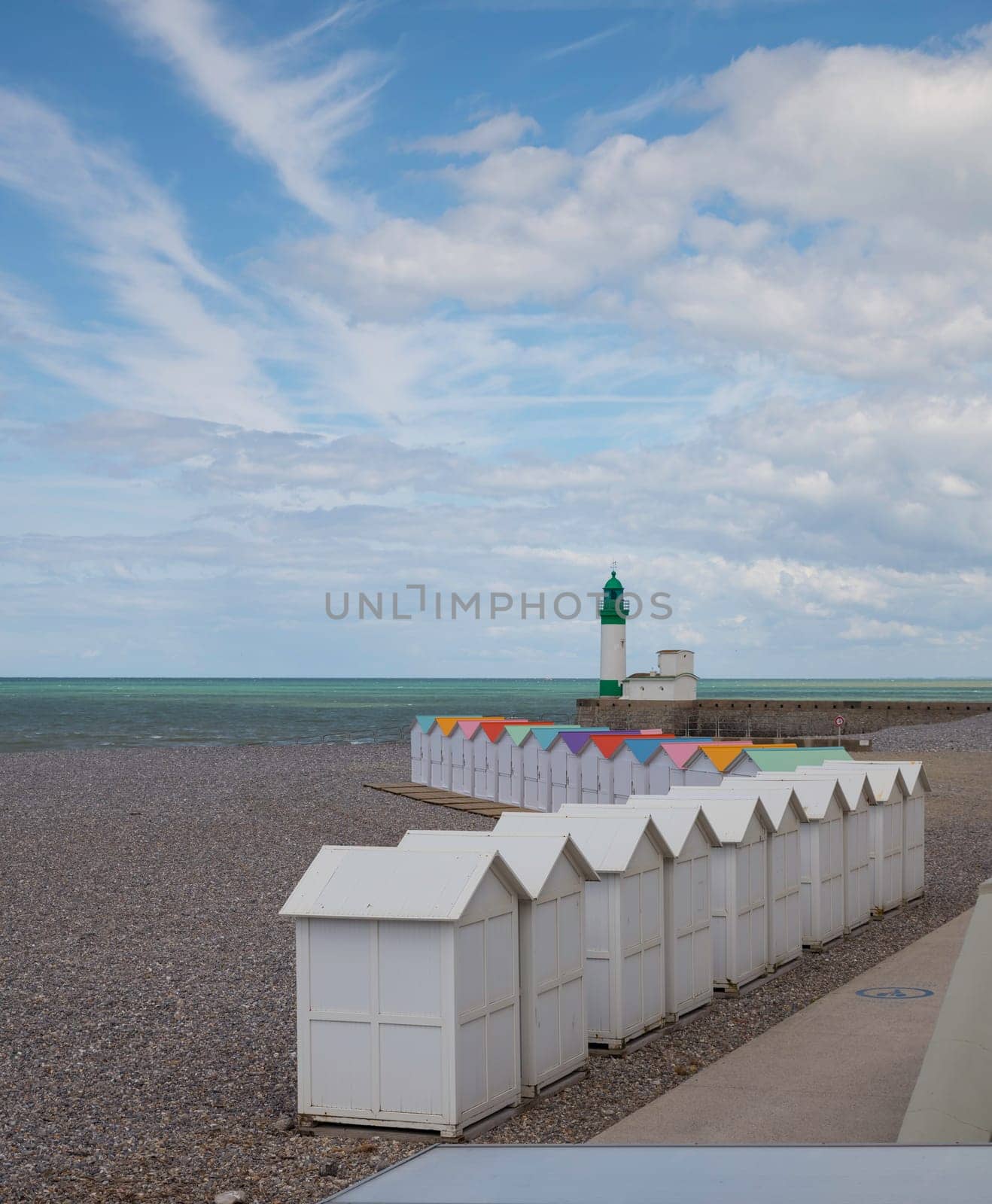 wooden beach houses with different colored roofs on the beach of le treport in France Normandy with the lighthouse at the background